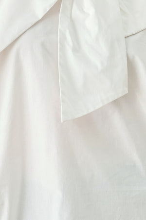 A woman wearing a white long-sleeve blouse with a large draped bow at the collar | FREEMARKET