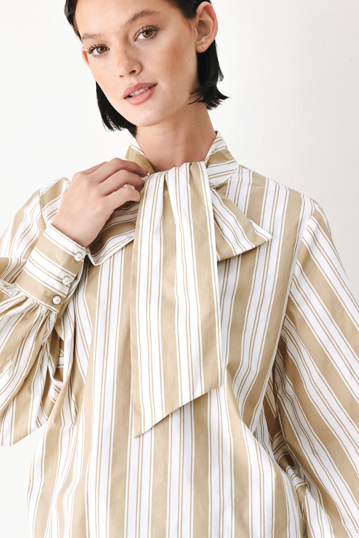 A model wearing a khaki beige and white vertically striped blouse with a large ruffled bow at the collar and voluminous long sleeves | FREEMARKET