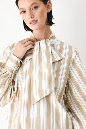 A model wearing a khaki beige and white vertically striped blouse with a large ruffled bow at the collar and voluminous long sleeves | FREEMARKET