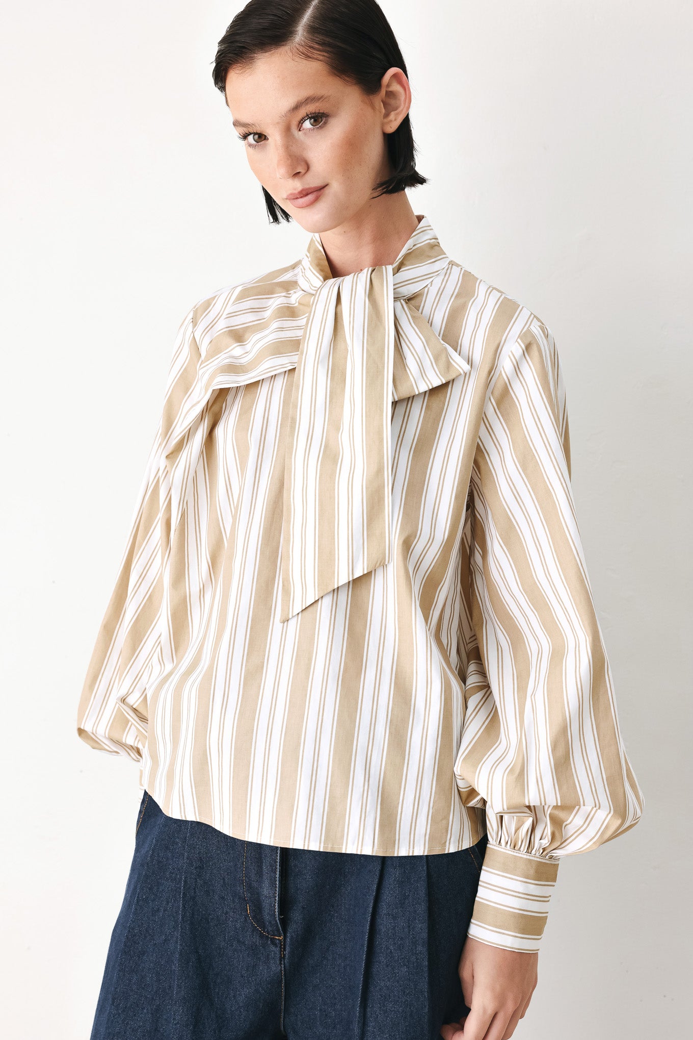 A model wearing a khaki beige and white vertically striped blouse with a large ruffled bow at the collar and voluminous long sleeves | FREEMARKET