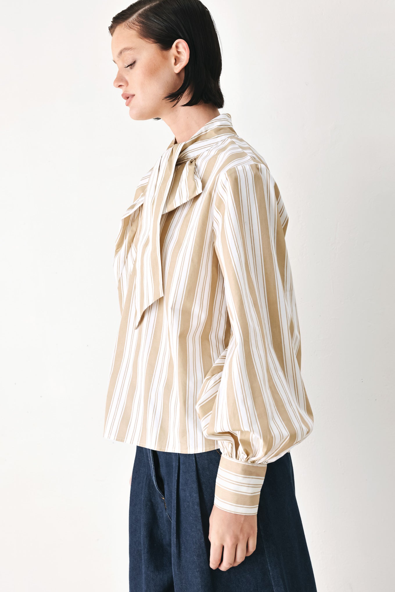 A model wearing a khaki beige and white vertically striped blouse with a large ruffled bow at the collar and voluminous long sleeves | FREEMARKET