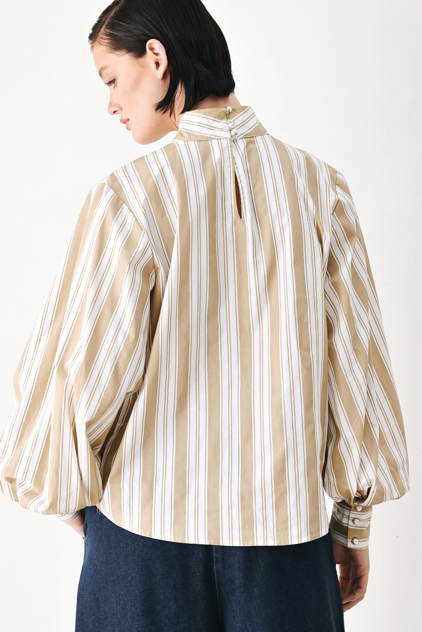 A model wearing a khaki beige and white vertically striped blouse with a large ruffled bow at the collar and voluminous long sleeves | FREEMARKET