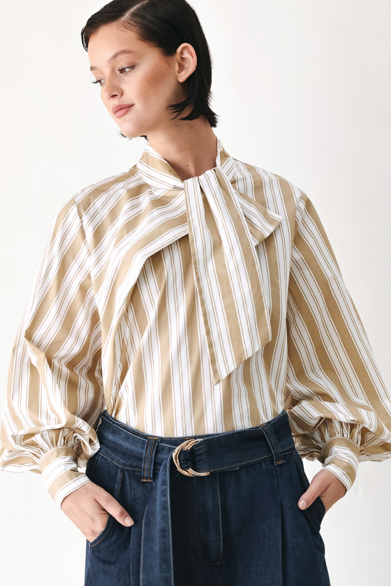A model wearing a khaki beige and white vertically striped blouse with a large ruffled bow at the collar and voluminous long sleeves | FREEMARKET