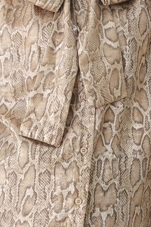 A woman modeling a long-sleeve brown and gold snake-patterned blouse with a tie-neck detail | FREEMARKET