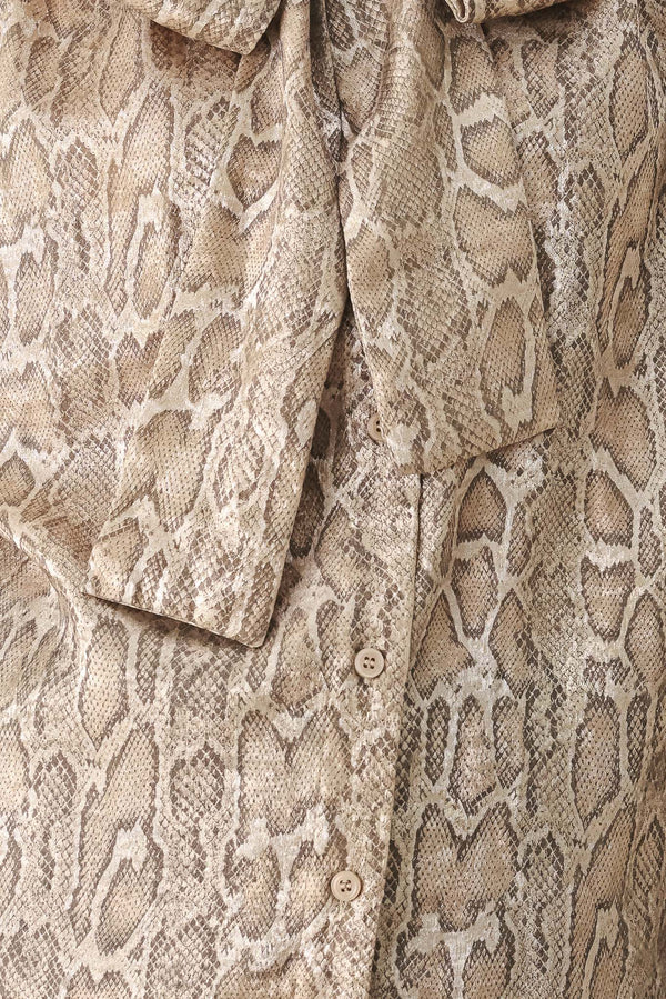 A woman modeling a long-sleeve brown and gold snake-patterned blouse with a tie-neck detail | FREEMARKET