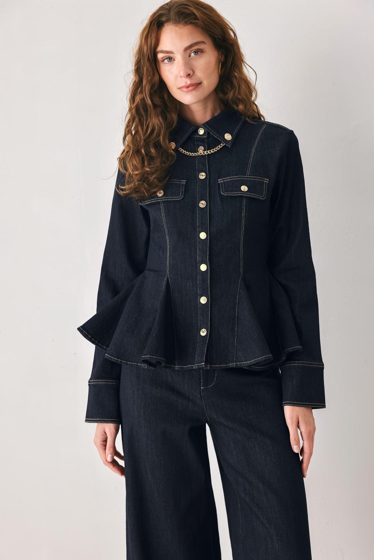 Woman wearing a navy blue denim long sleep button up top with a peplum waist, a collar and chain connected to the corners of the collar | FREEMARKET