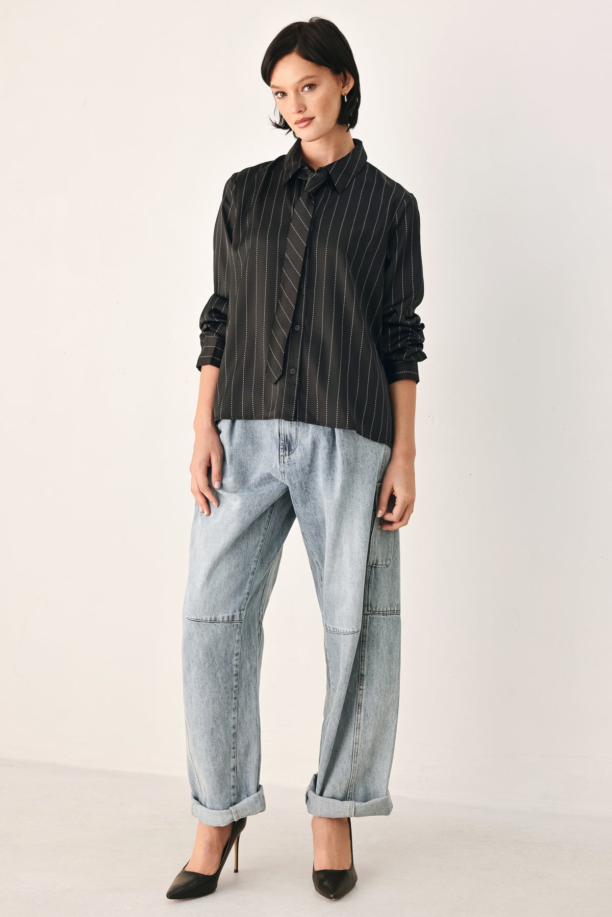 A woman wearing a black long-sleeve button-up shirt with thin white vertical pinstripes, styled with a matching striped tie | FREEMARKET