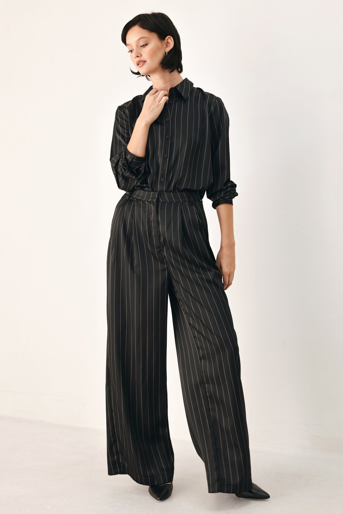 A woman wearing a black long-sleeve button-up shirt with thin white vertical pinstripes, styled with a matching striped tie | FREEMARKET