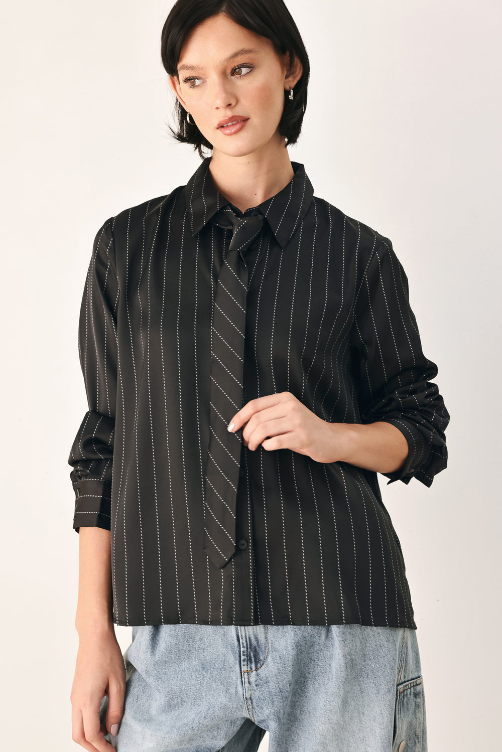 A woman wearing a black long-sleeve button-up shirt with thin white vertical pinstripes, styled with a matching striped tie | FREEMARKET
