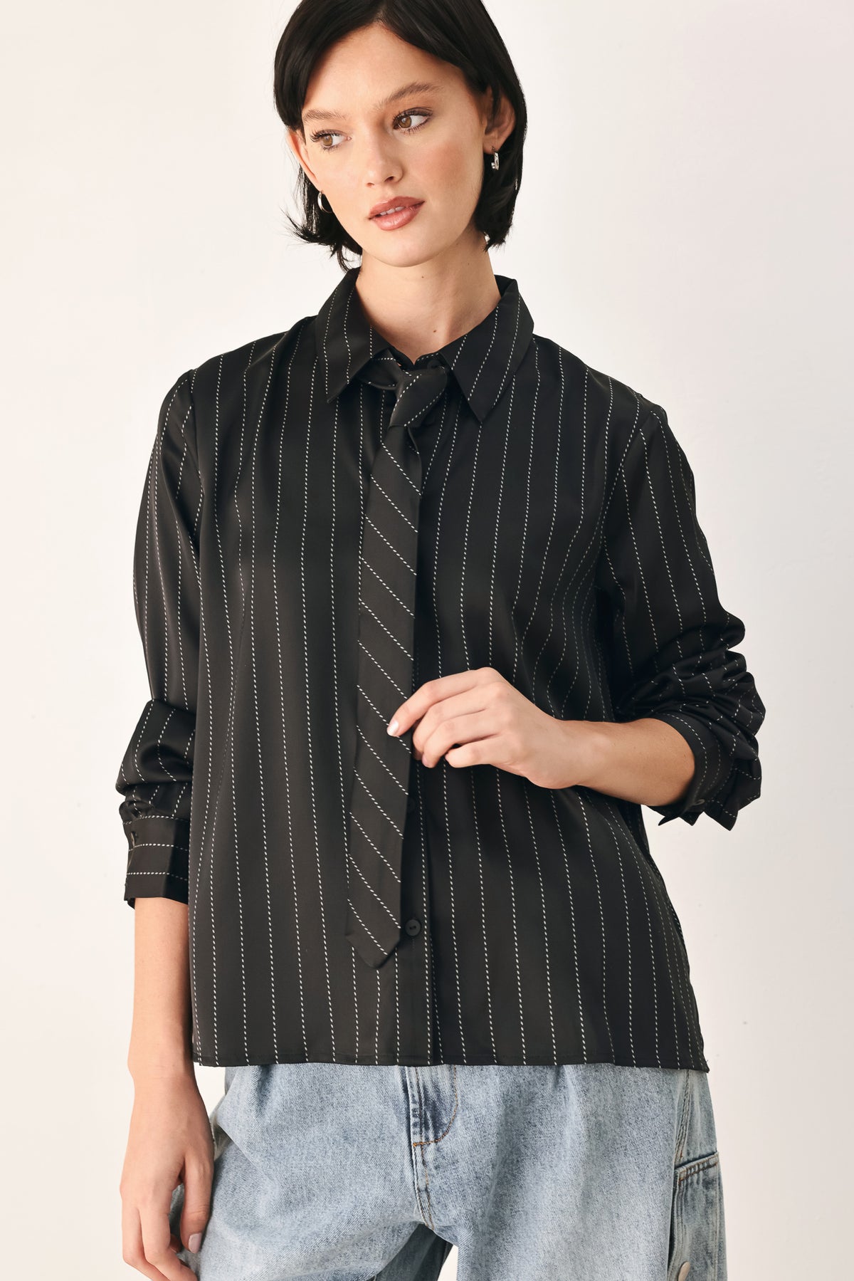 A woman wearing a black long-sleeve button-up shirt with thin white vertical pinstripes, styled with a matching striped tie | FREEMARKET