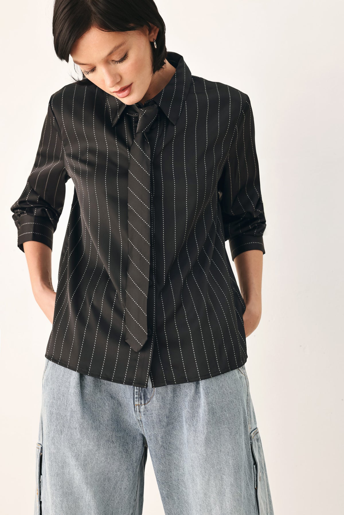 A woman wearing a black long-sleeve button-up shirt with thin white vertical pinstripes, styled with a matching striped tie | FREEMARKET