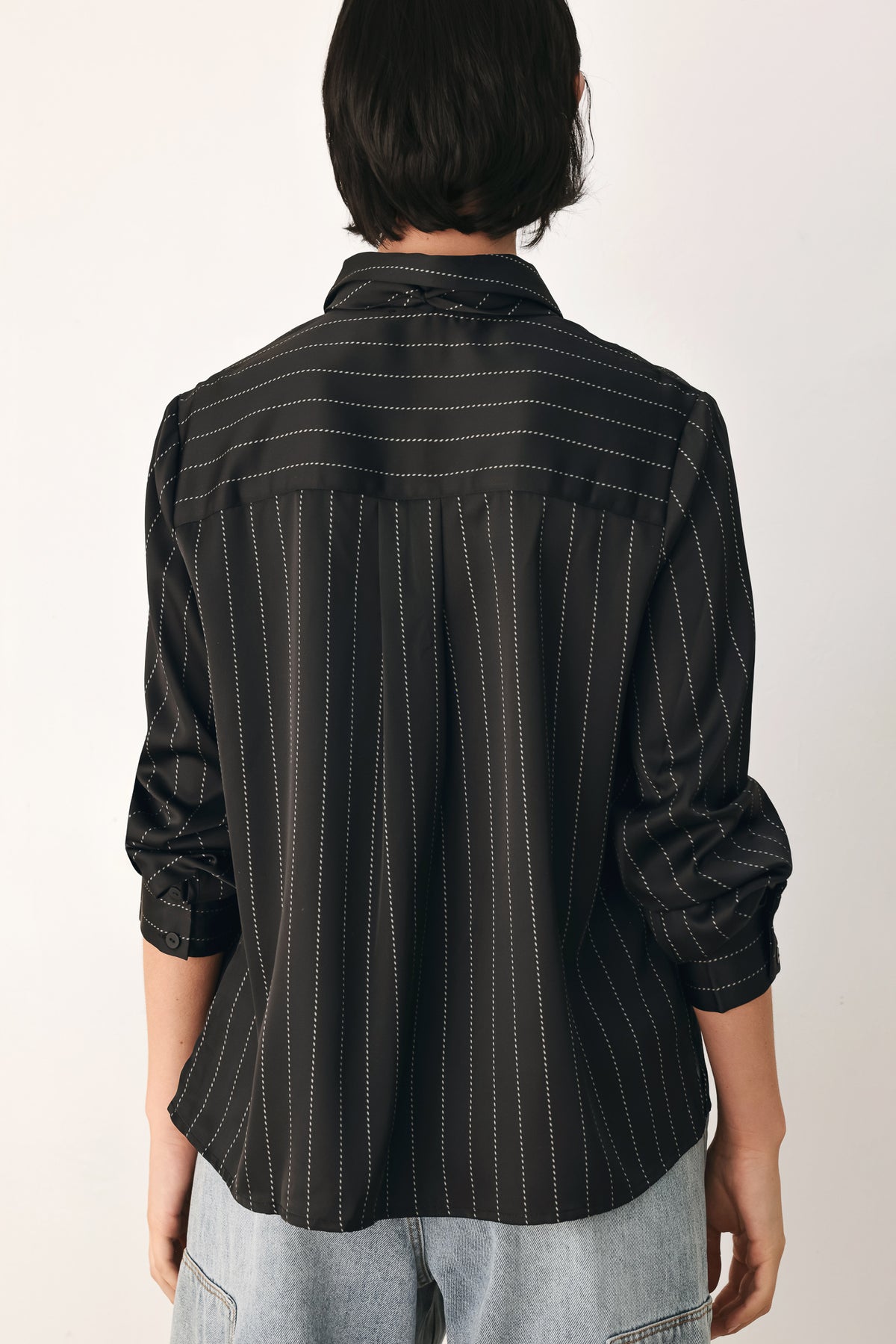 A woman wearing a black long-sleeve button-up shirt with thin white vertical pinstripes, styled with a matching striped tie | FREEMARKET