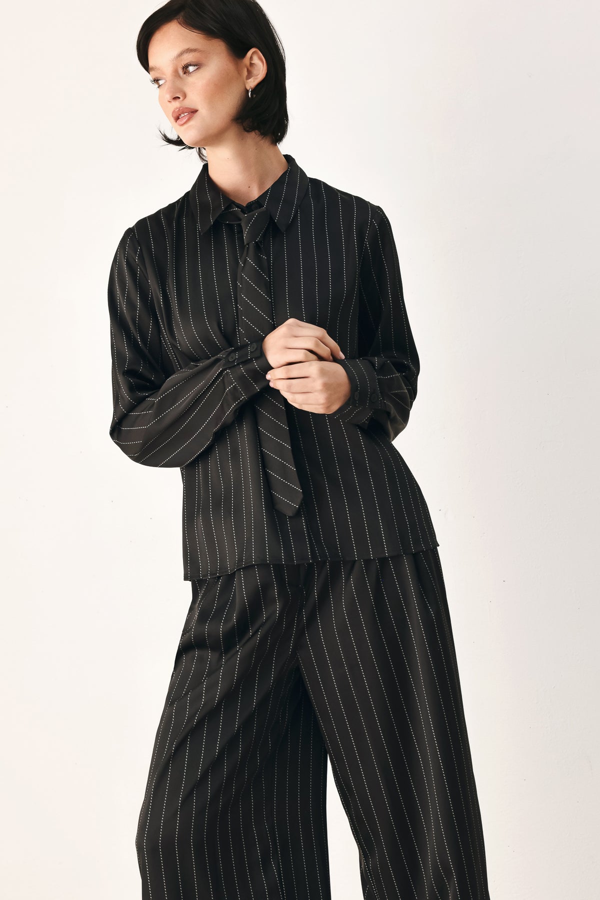 A woman wearing a black long-sleeve button-up shirt with thin white vertical pinstripes, styled with a matching striped tie | FREEMARKET
