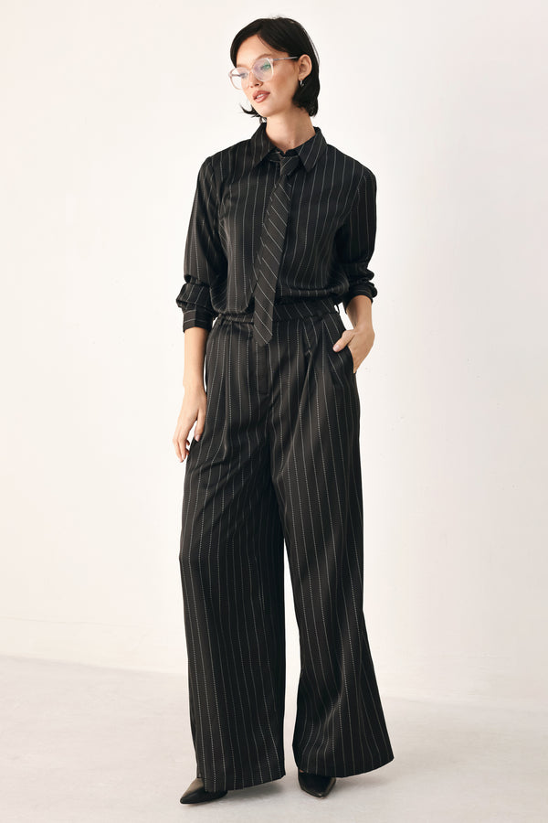 A woman wearing a black long-sleeve button-up shirt with thin white vertical pinstripes, styled with a matching striped tie | FREEMARKET