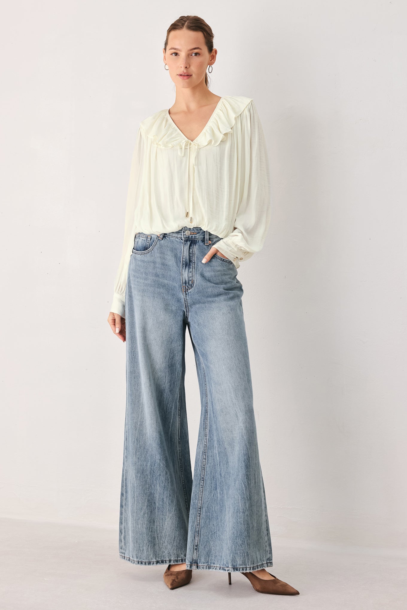 A woman wearing a cream-colored long-sleeve blouse with a ruffled collar and tie detail | FREEMARKET