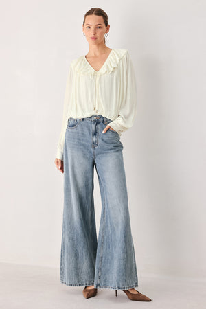A woman wearing a cream-colored long-sleeve blouse with a ruffled collar and tie detail | FREEMARKET