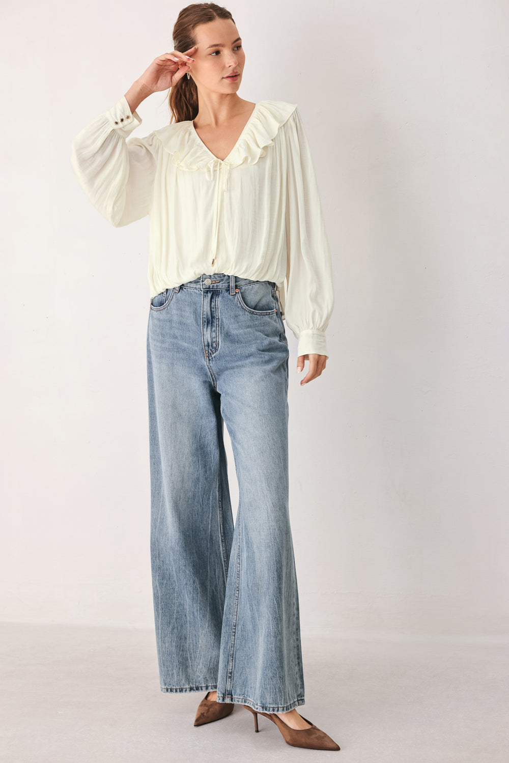 A woman wearing a cream-colored long-sleeve blouse with a ruffled collar and tie detail | FREEMARKET