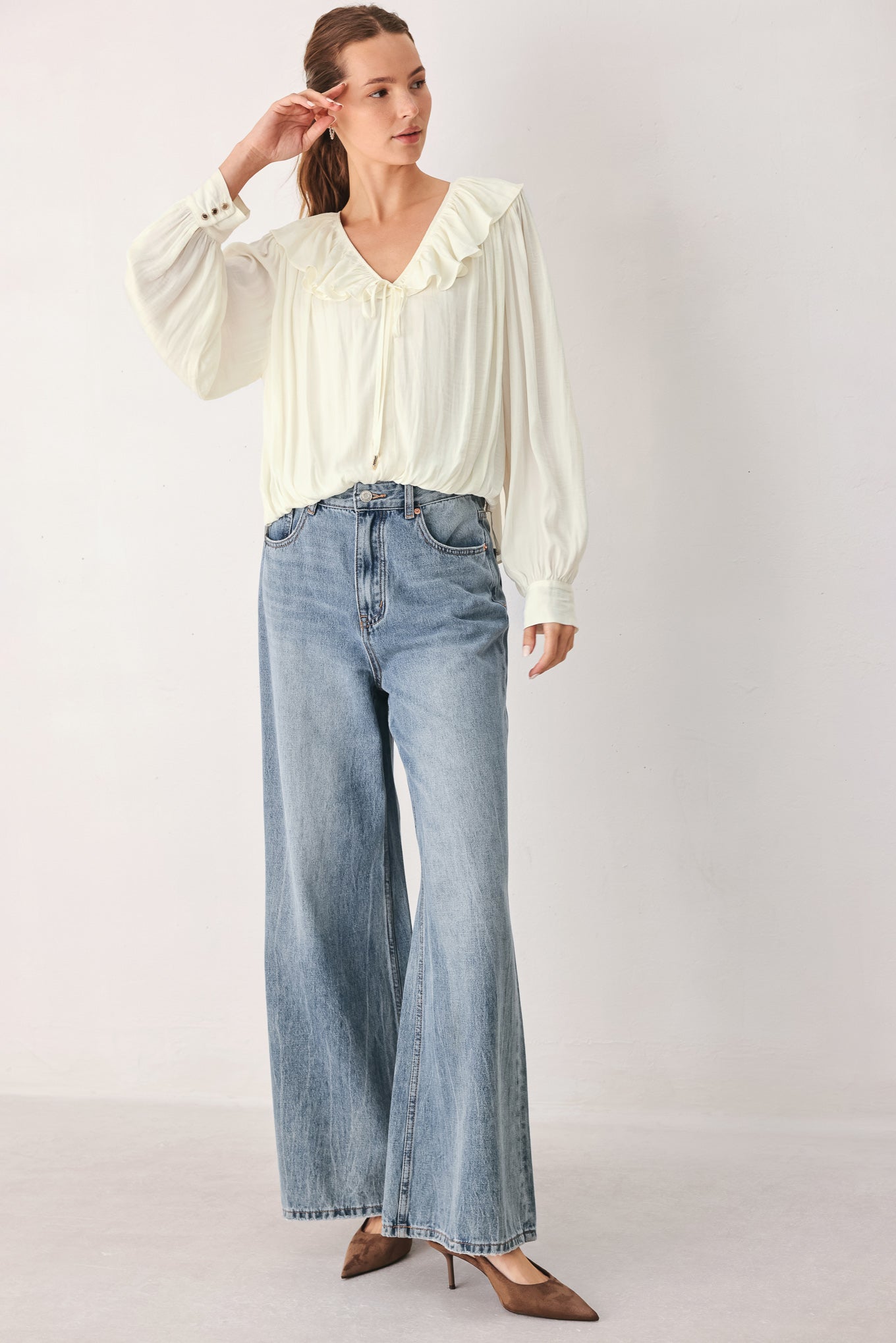 A woman wearing a cream-colored long-sleeve blouse with a ruffled collar and tie detail | FREEMARKET