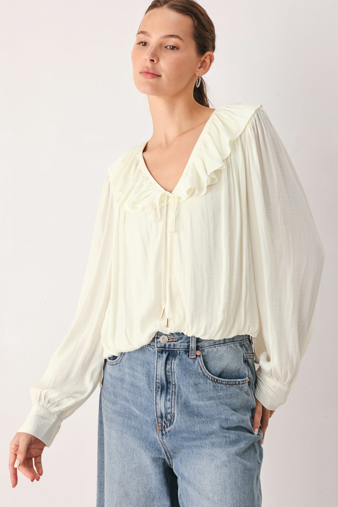 A woman wearing a cream-colored long-sleeve blouse with a ruffled collar and tie detail | FREEMARKET