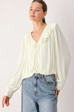 A woman wearing a cream-colored long-sleeve blouse with a ruffled collar and tie detail | FREEMARKET