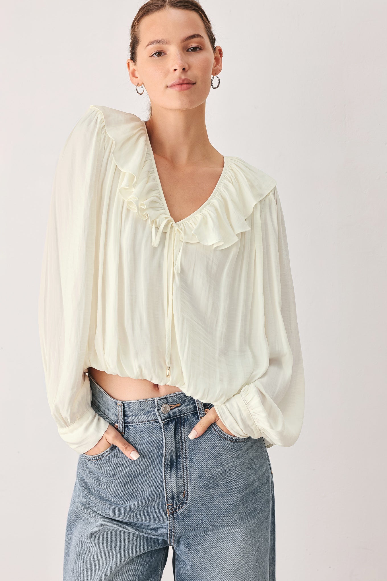 A woman wearing a cream-colored long-sleeve blouse with a ruffled collar and tie detail | FREEMARKET