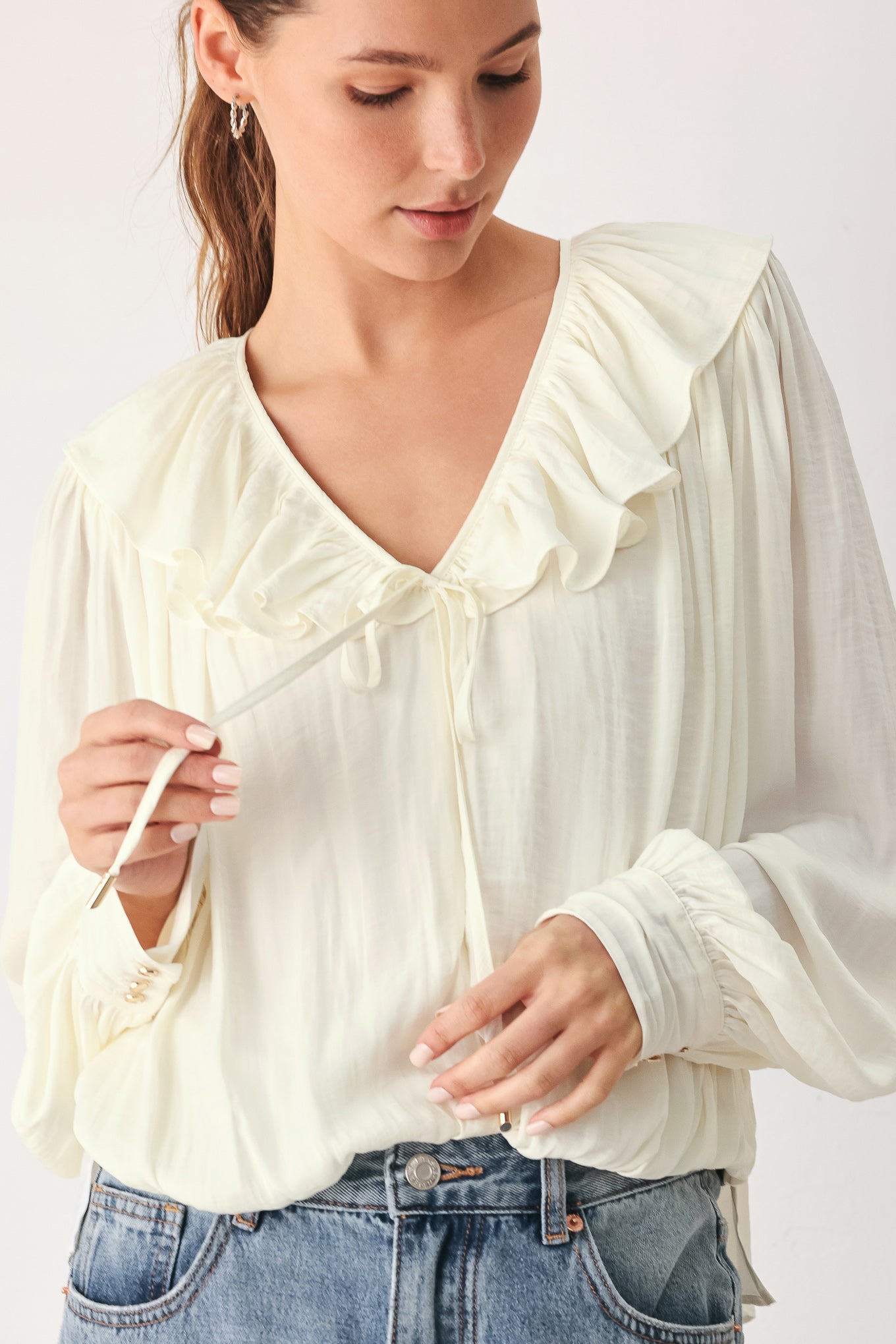 A woman wearing a cream-colored long-sleeve blouse with a ruffled collar and tie detail | FREEMARKET