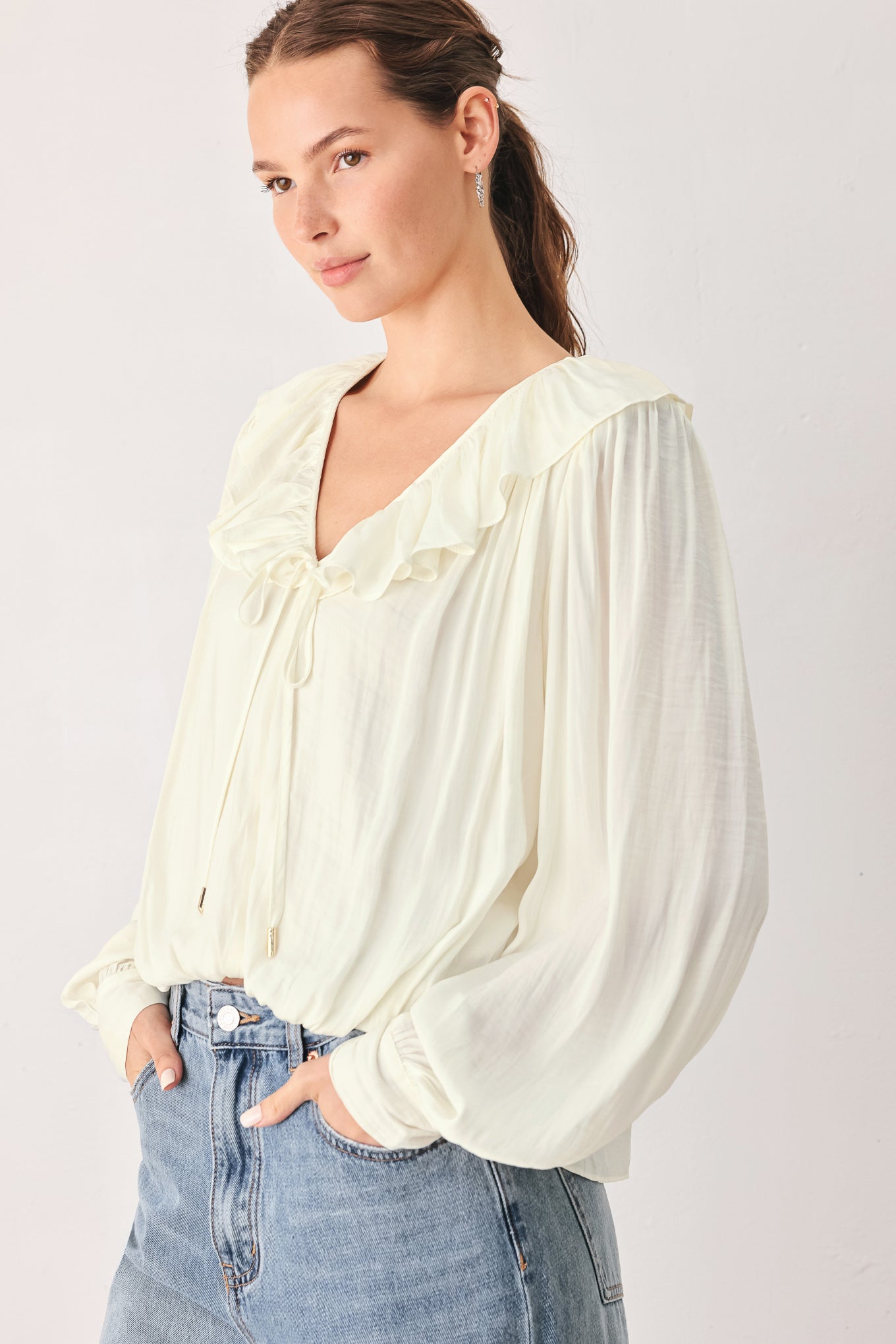 A woman wearing a cream-colored long-sleeve blouse with a ruffled collar and tie detail | FREEMARKET
