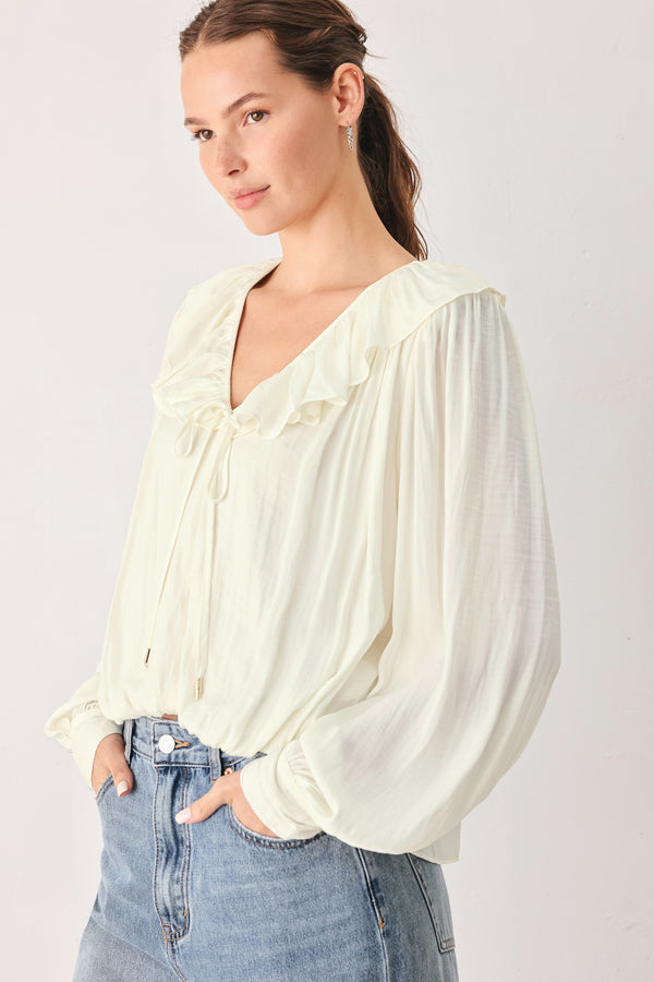 A woman wearing a cream-colored long-sleeve blouse with a ruffled collar and tie detail | FREEMARKET
