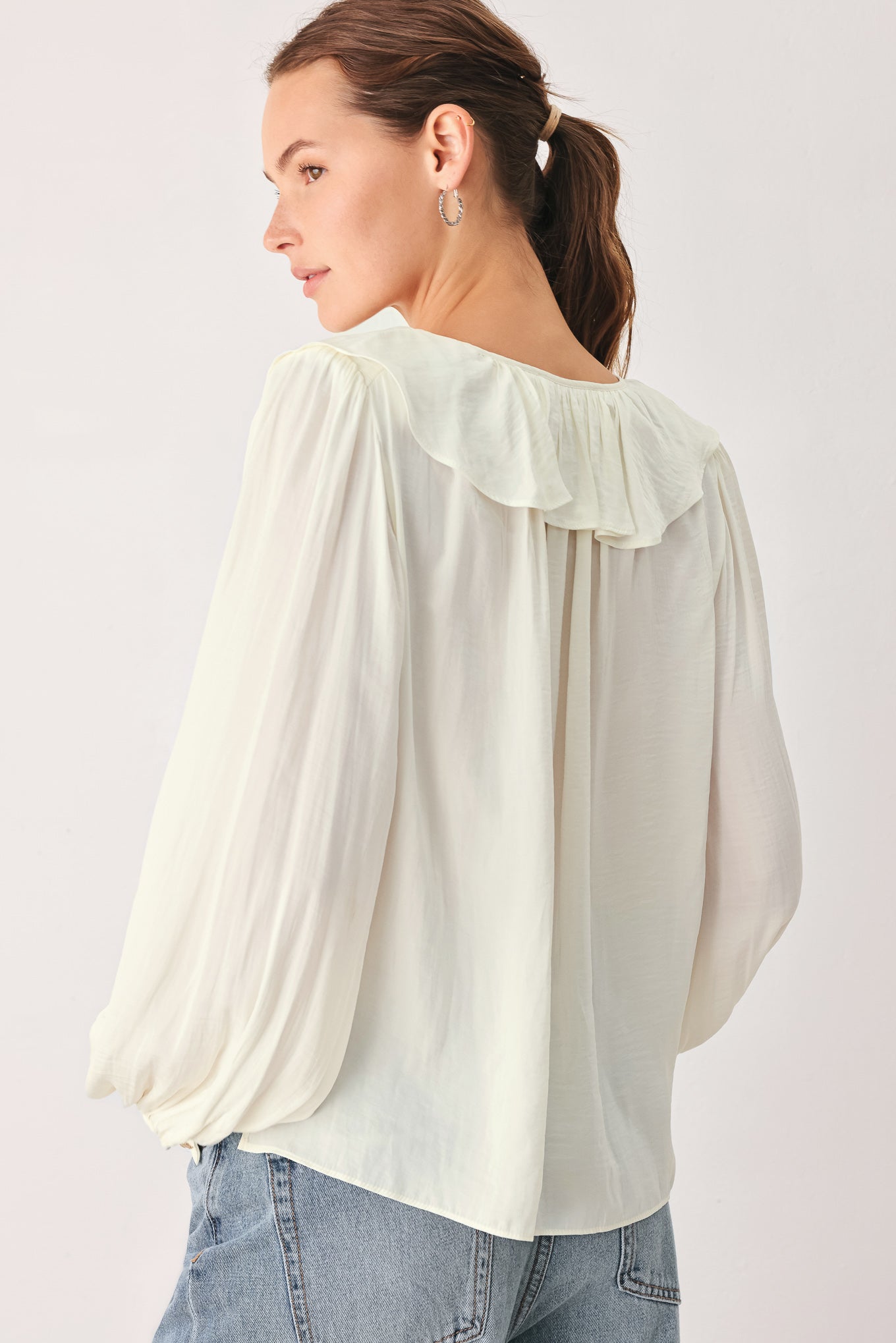 A woman wearing a cream-colored long-sleeve blouse with a ruffled collar and tie detail | FREEMARKET