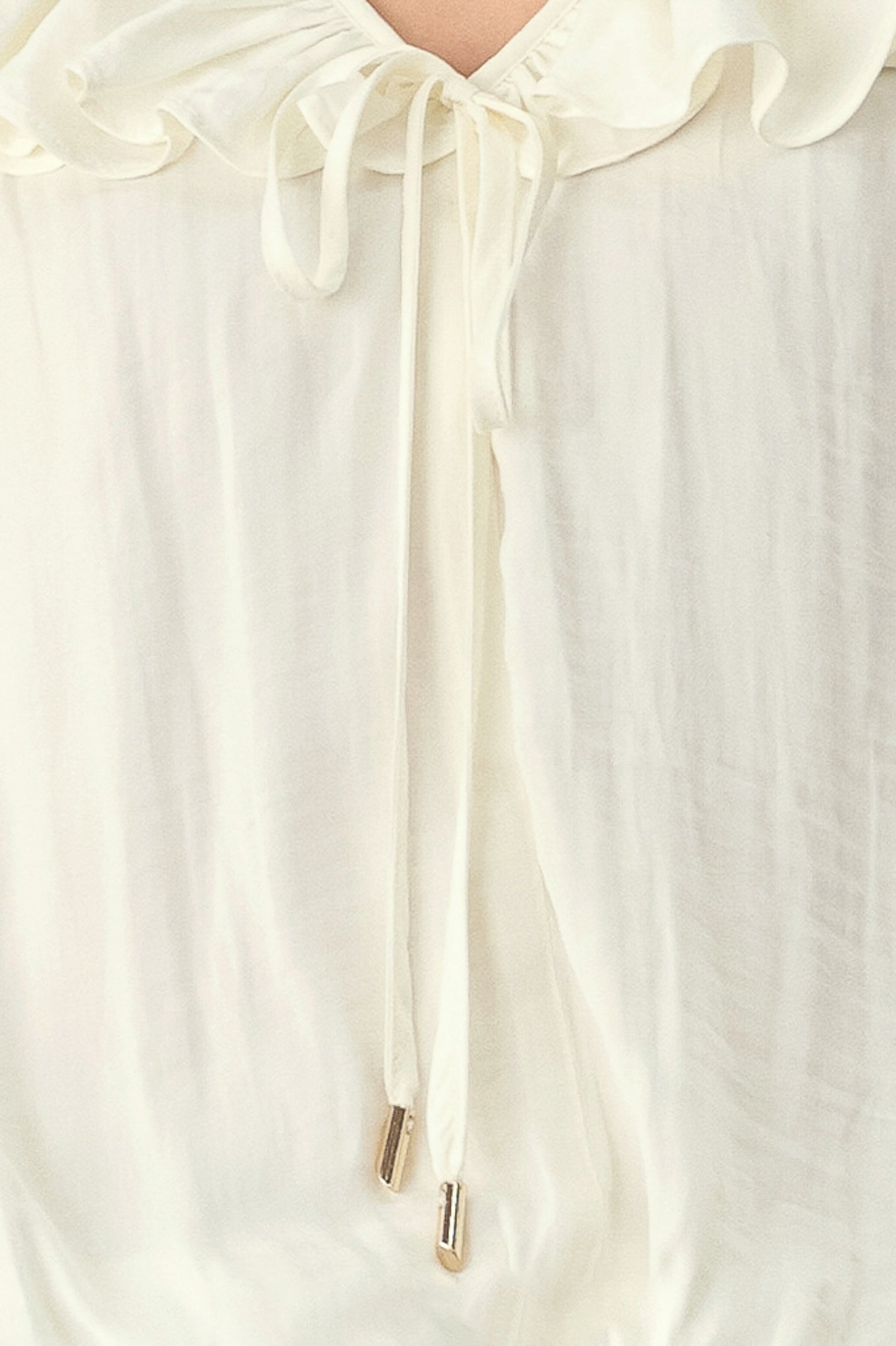 A woman wearing a cream-colored long-sleeve blouse with a ruffled collar and tie detail | FREEMARKET