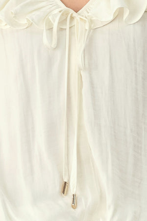 A woman wearing a cream-colored long-sleeve blouse with a ruffled collar and tie detail | FREEMARKET