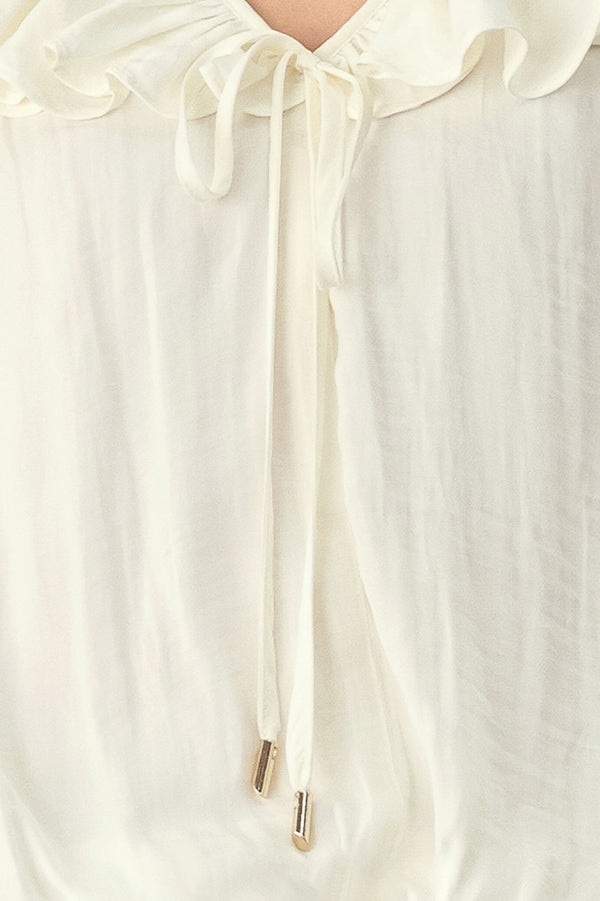 A woman wearing a cream-colored long-sleeve blouse with a ruffled collar and tie detail | FREEMARKET