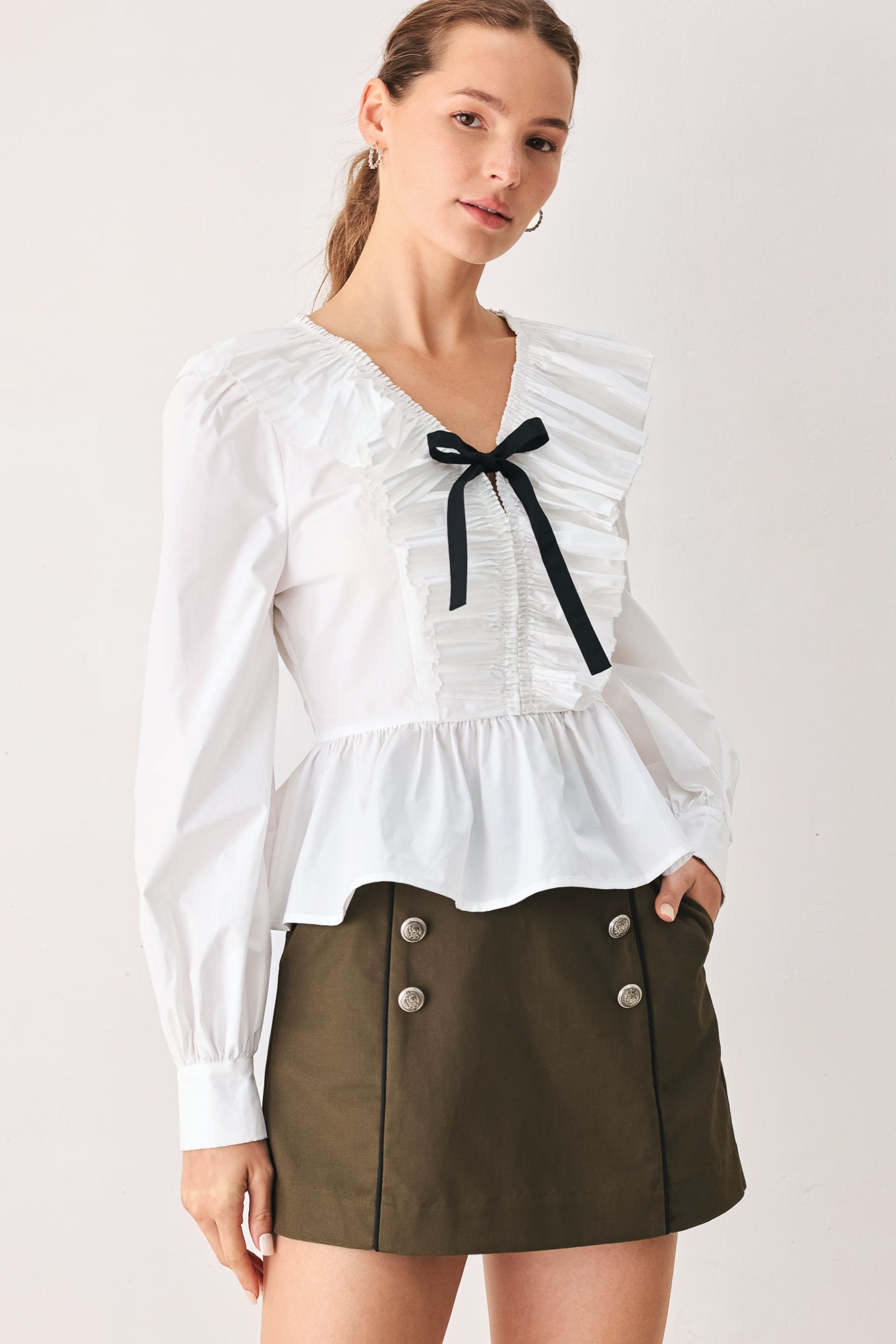 A woman wearing a white long-sleeve blouse with a ruffled V-neck, gathered waist, and a black ribbon bow at the center | FREEMARKET