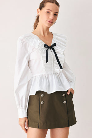 A woman wearing a white long-sleeve blouse with a ruffled V-neck, gathered waist, and a black ribbon bow at the center | FREEMARKET