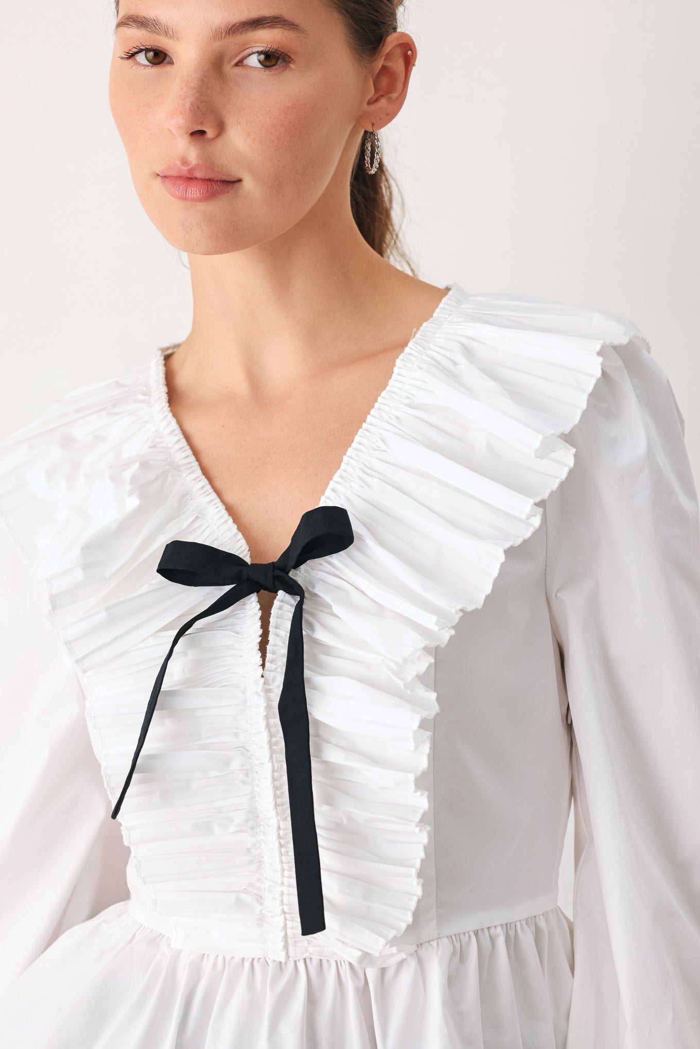 A woman wearing a white long-sleeve blouse with a ruffled V-neck, gathered waist, and a black ribbon bow at the center | FREEMARKET