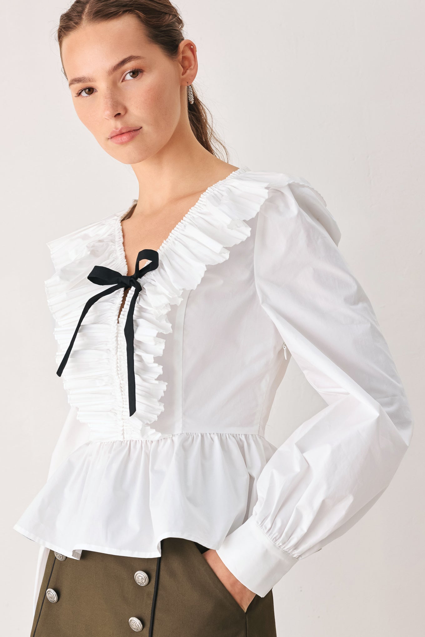 A woman wearing a white long-sleeve blouse with a ruffled V-neck, gathered waist, and a black ribbon bow at the center | FREEMARKET