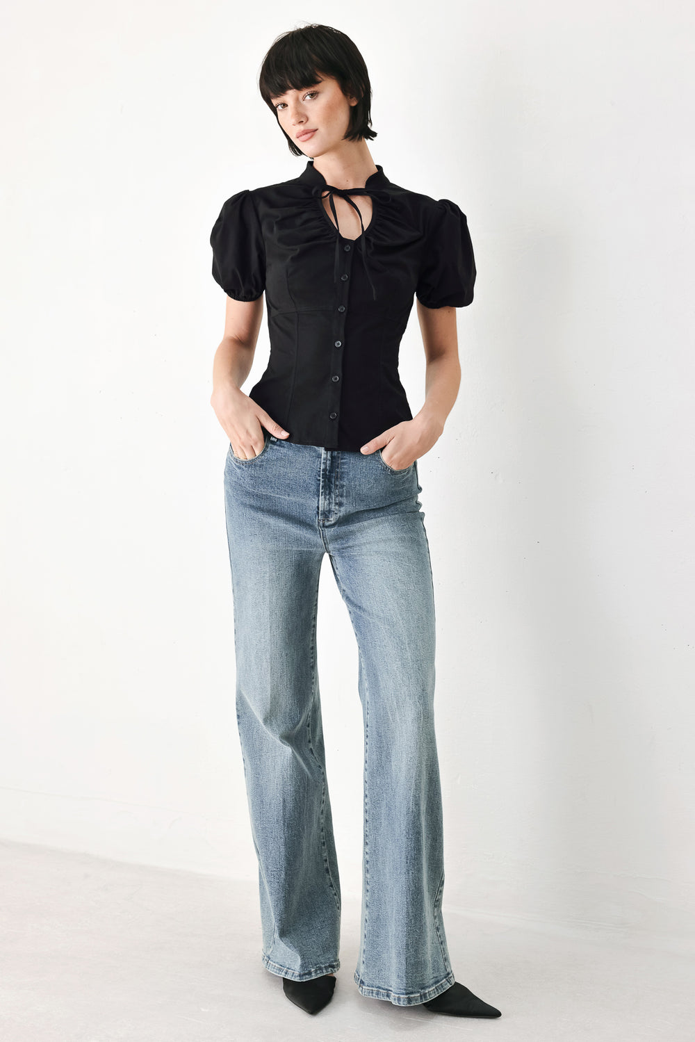 A woman wearing a black short-sleeve blouse with puff sleeves, a ruffled collar, and a keyhole cutout at the neckline | FREEMARKET