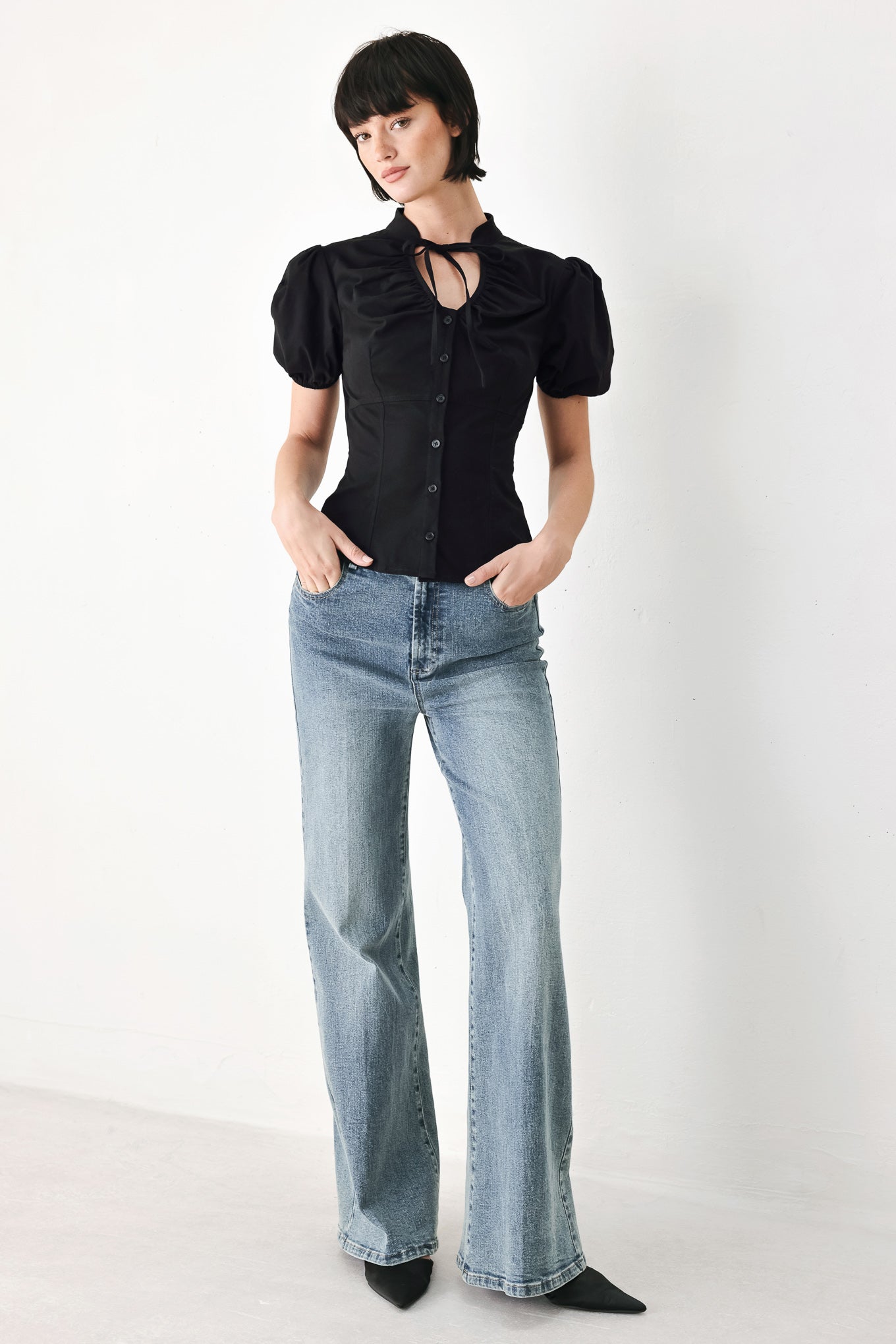 A woman wearing a black short-sleeve blouse with puff sleeves, a ruffled collar, and a keyhole cutout at the neckline | FREEMARKET