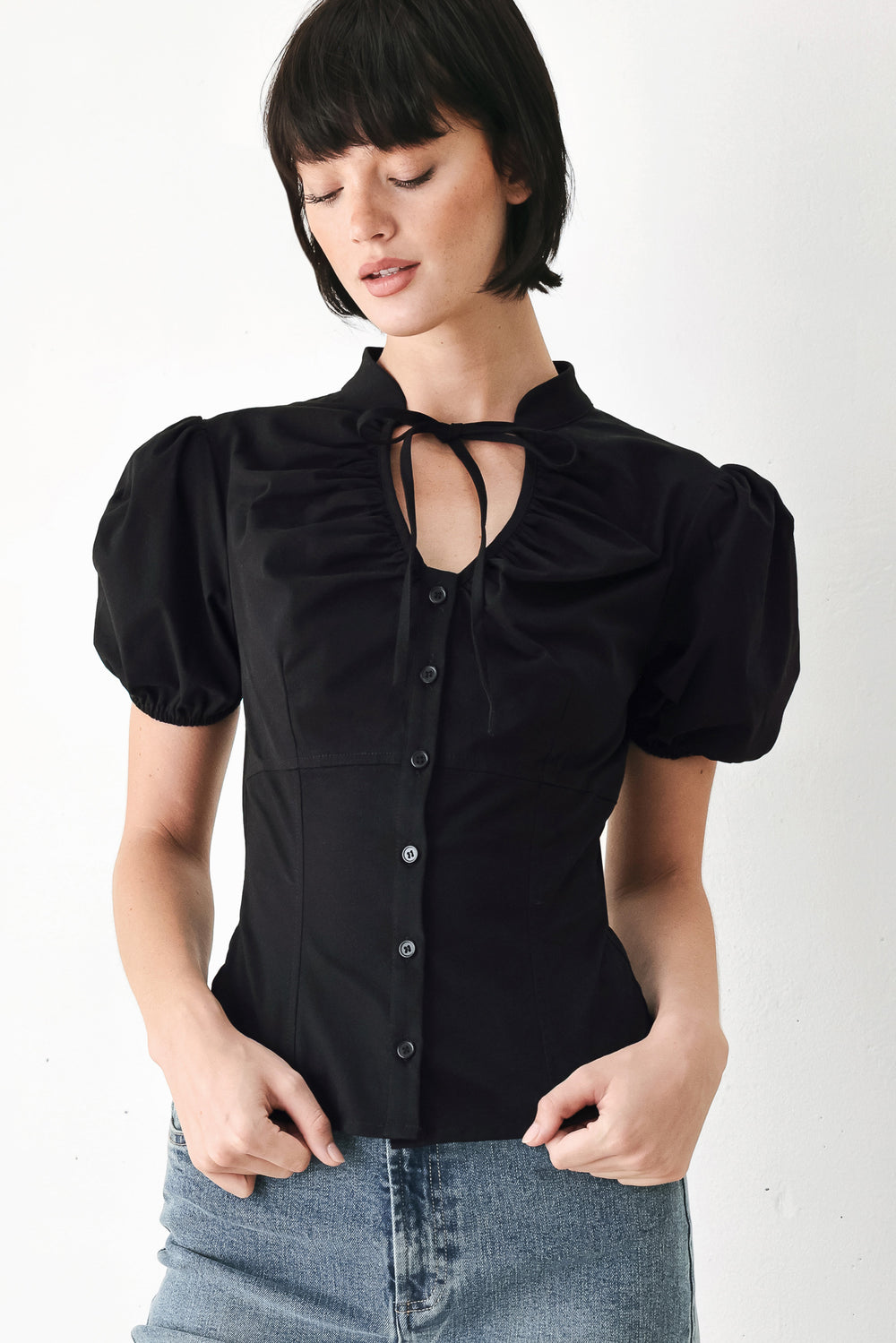 A woman wearing a black short-sleeve blouse with puff sleeves, a ruffled collar, and a keyhole cutout at the neckline | FREEMARKET