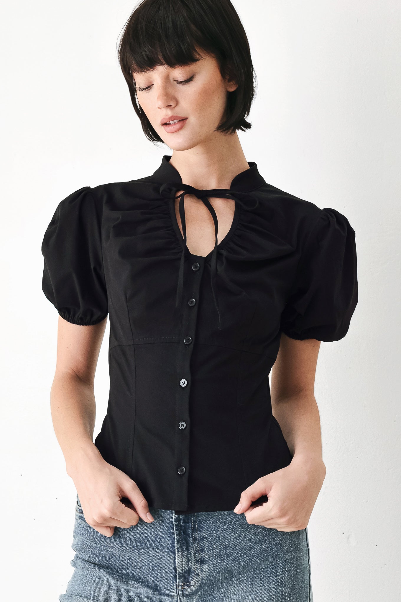 A woman wearing a black short-sleeve blouse with puff sleeves, a ruffled collar, and a keyhole cutout at the neckline | FREEMARKET