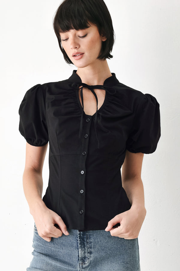 A woman wearing a black short-sleeve blouse with puff sleeves, a ruffled collar, and a keyhole cutout at the neckline | FREEMARKET
