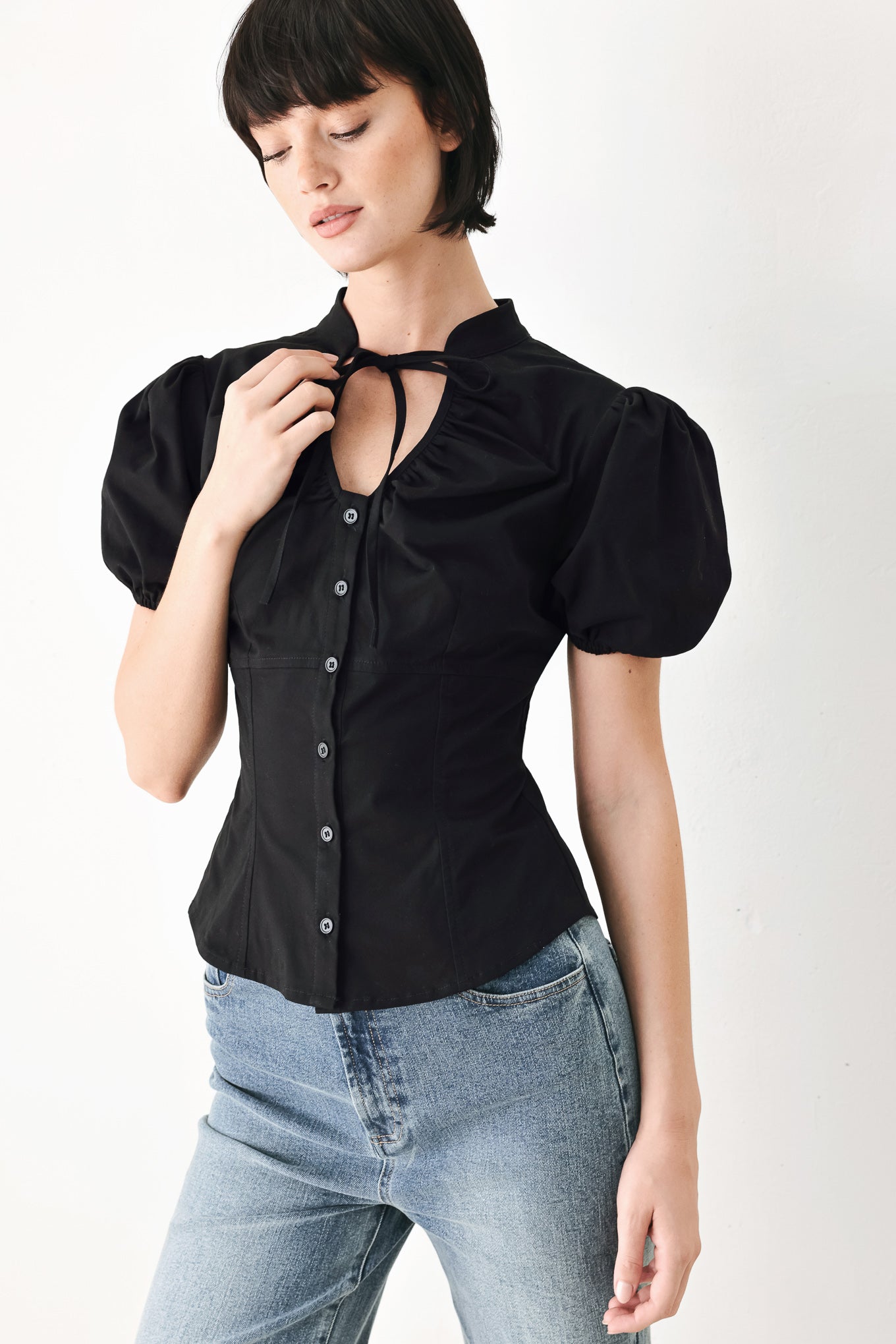 A woman wearing a black short-sleeve blouse with puff sleeves, a ruffled collar, and a keyhole cutout at the neckline | FREEMARKET