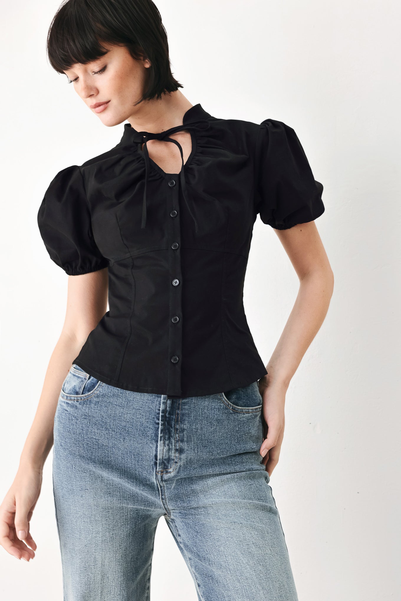 A woman wearing a black short-sleeve blouse with puff sleeves, a ruffled collar, and a keyhole cutout at the neckline | FREEMARKET
