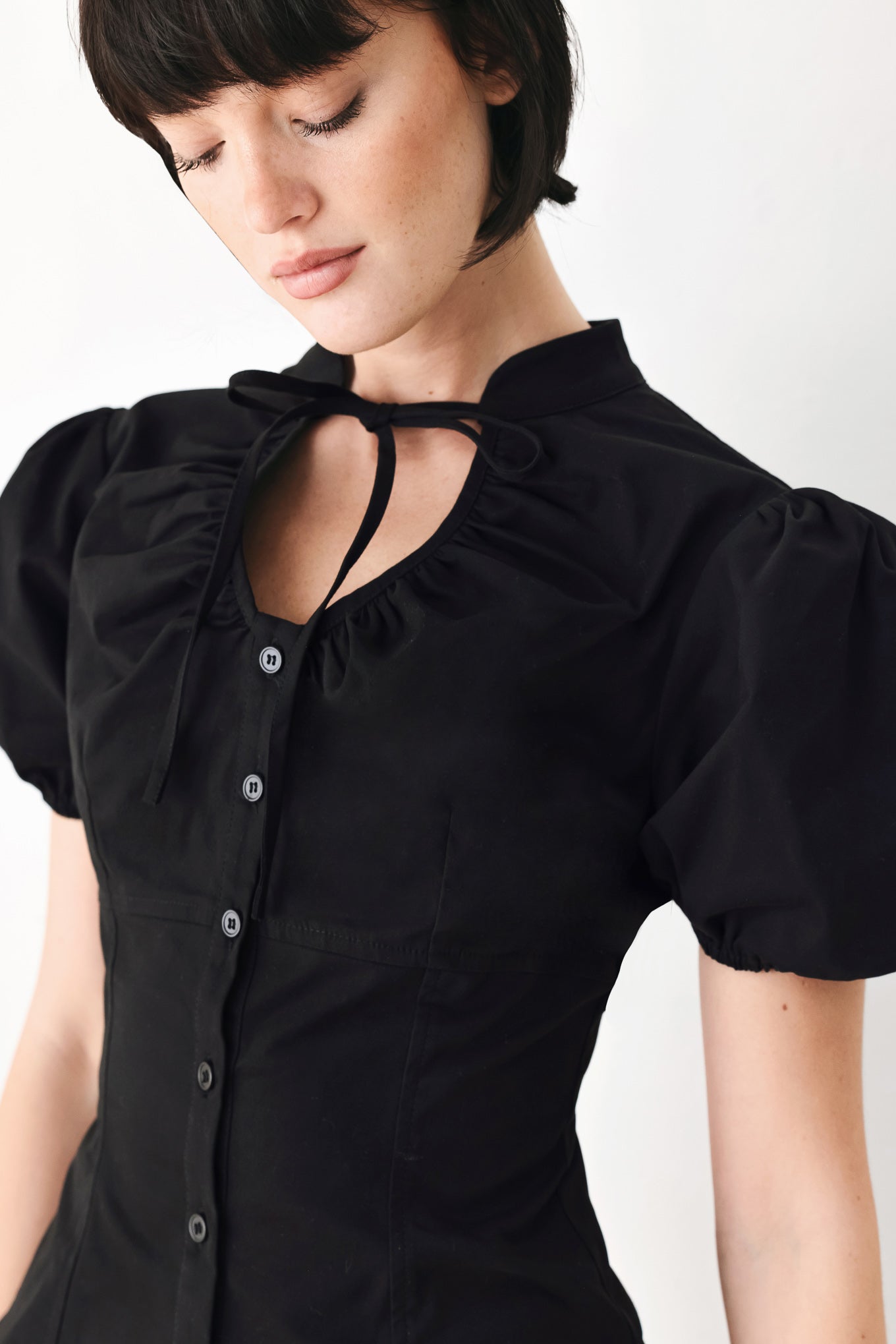 A woman wearing a black short-sleeve blouse with puff sleeves, a ruffled collar, and a keyhole cutout at the neckline | FREEMARKET