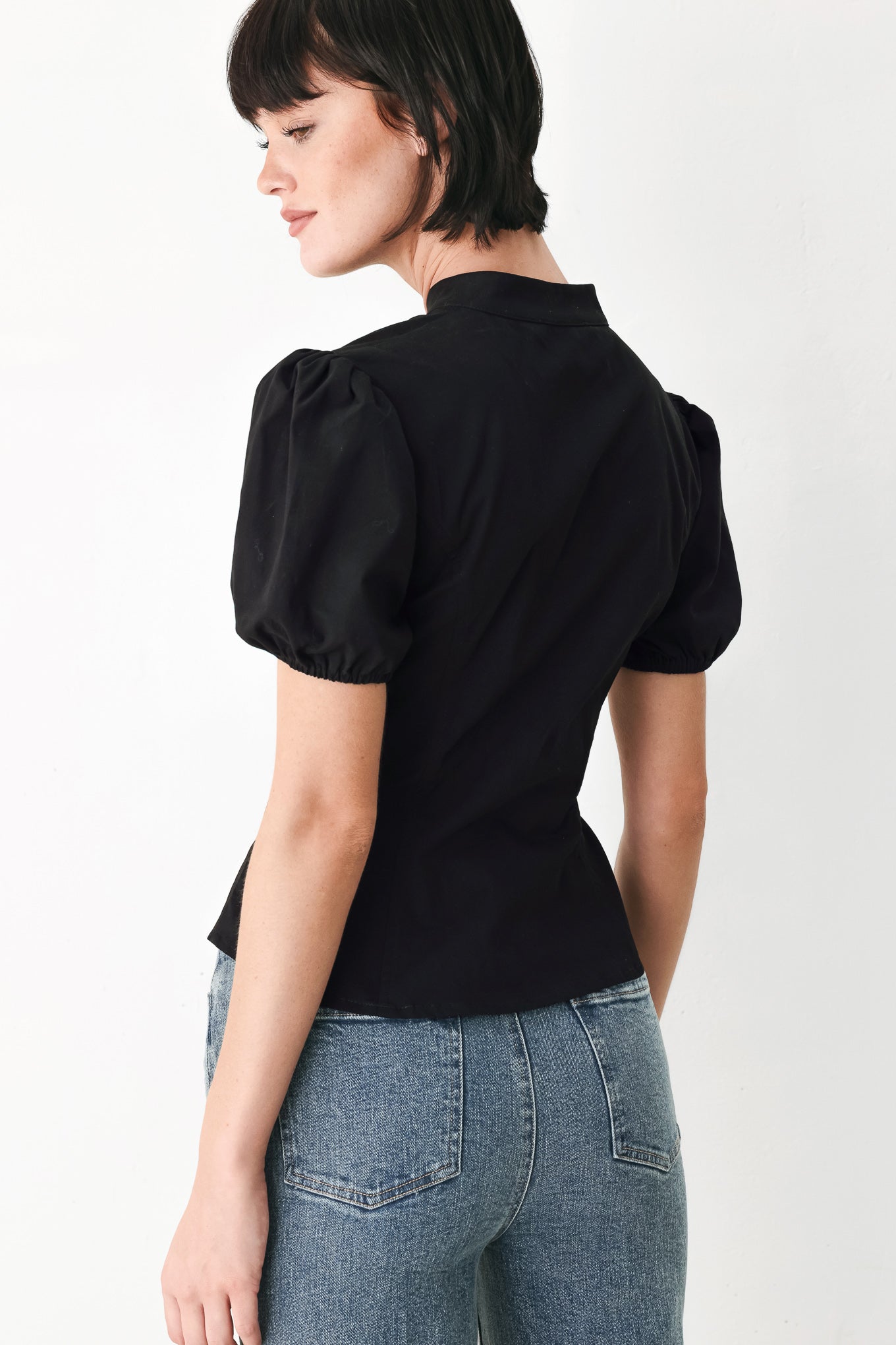 A woman wearing a black short-sleeve blouse with puff sleeves, a ruffled collar, and a keyhole cutout at the neckline | FREEMARKET