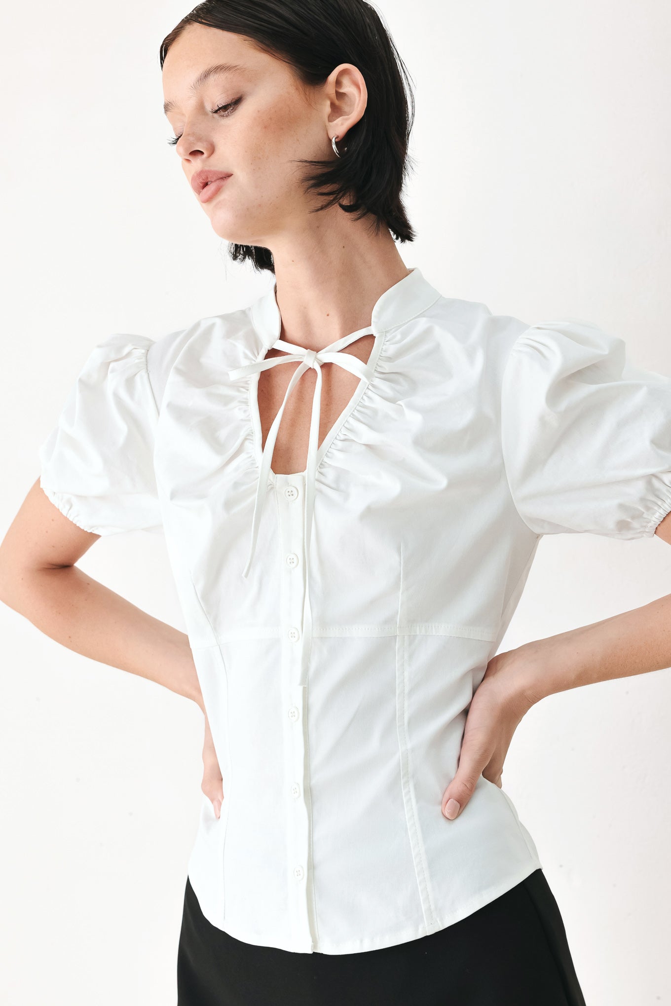 A woman wearing a white short-sleeve blouse with puff sleeves, a ruffled collar, and a keyhole cutout at the neckline | FREEMARKET