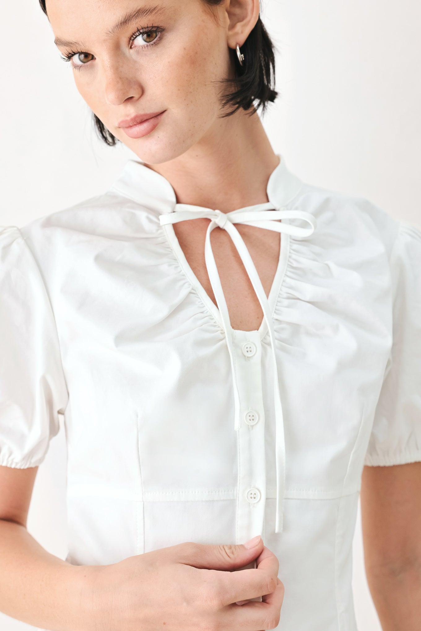 A woman wearing a white short-sleeve blouse with puff sleeves, a ruffled collar, and a keyhole cutout at the neckline | FREEMARKET