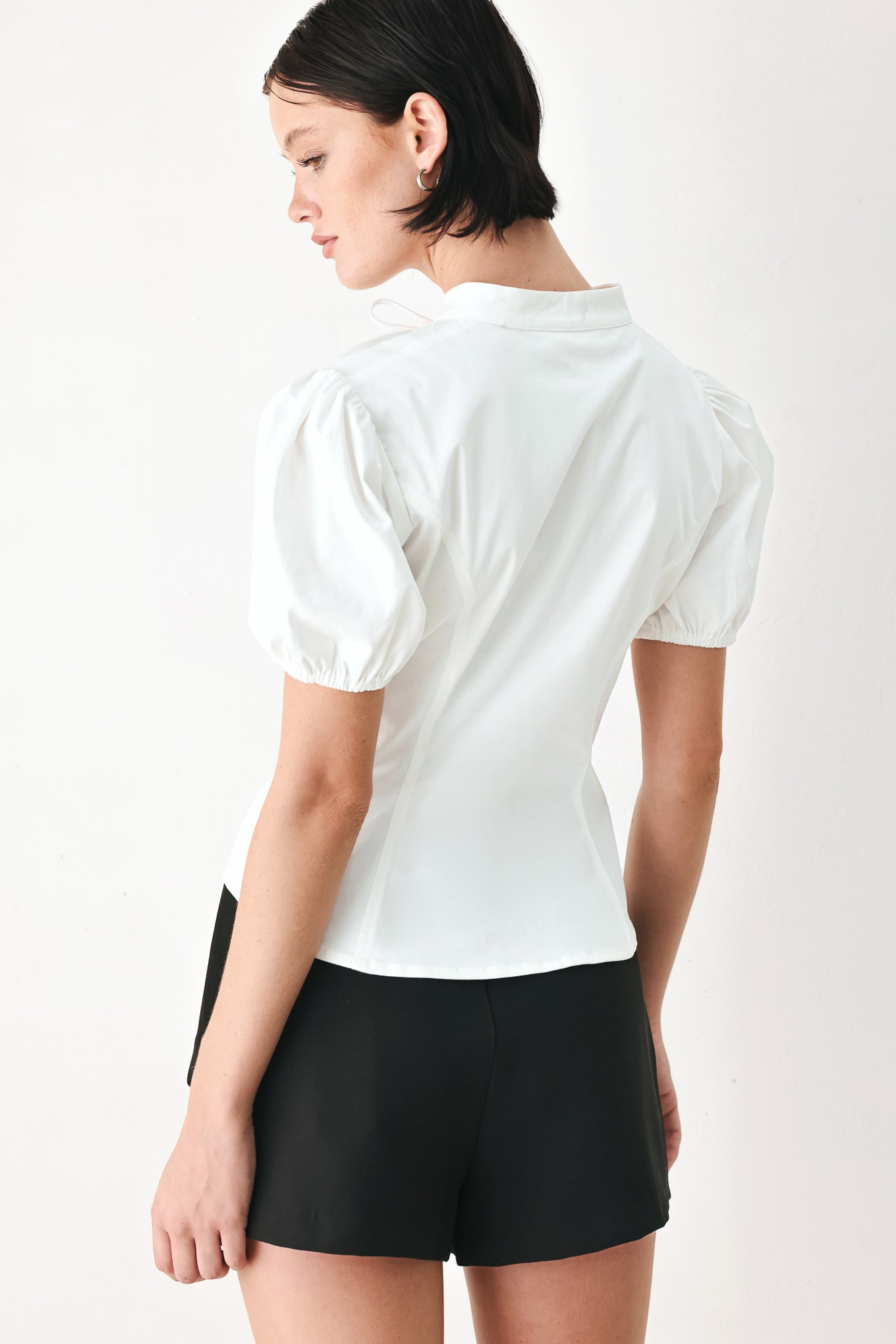 A woman wearing a white short-sleeve blouse with puff sleeves, a ruffled collar, and a keyhole cutout at the neckline | FREEMARKET