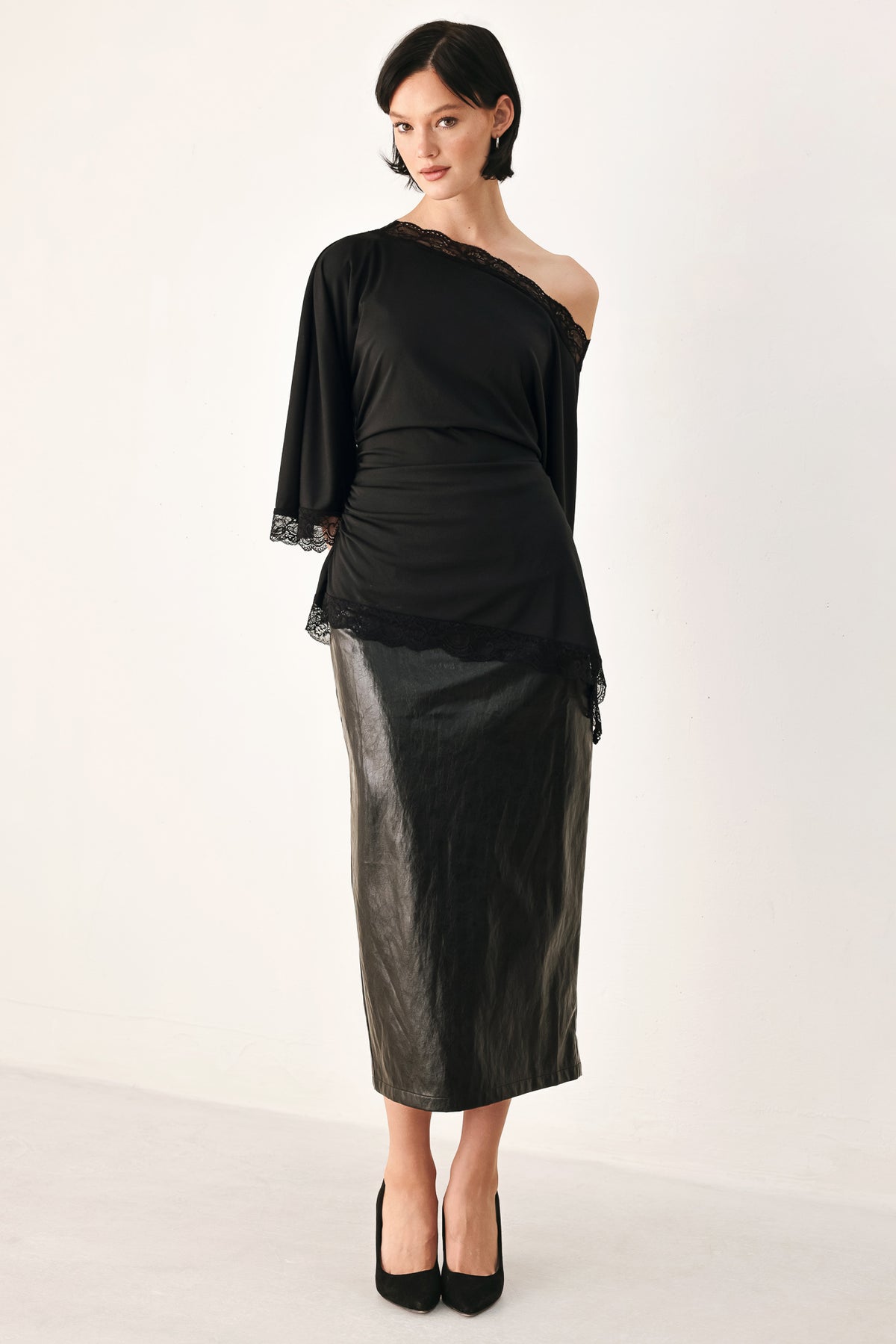 A model wearing a black asymmetrical off-the-shoulder top with black lace trim along the neckline, cuffs, and hem | FREEMARKET