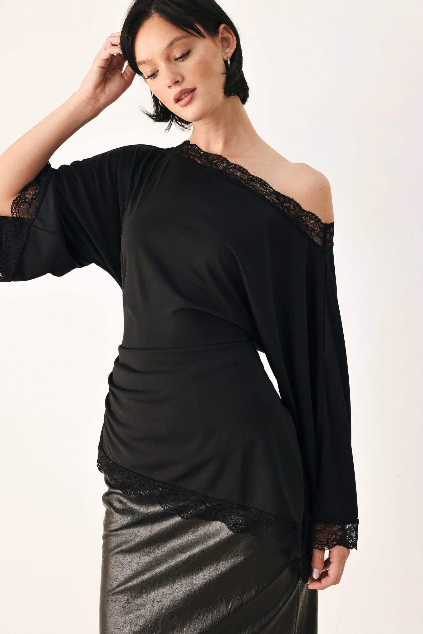 A model wearing a black asymmetrical off-the-shoulder top with black lace trim along the neckline, cuffs, and hem | FREEMARKET
